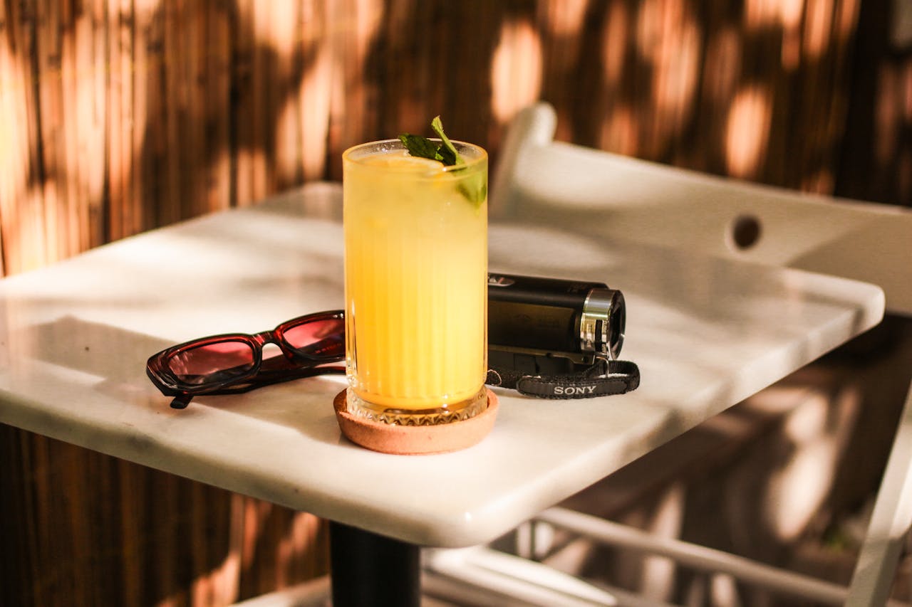 Lemonade with mint and lime on a sunlit table, surrounded by sunglasses and a camera.